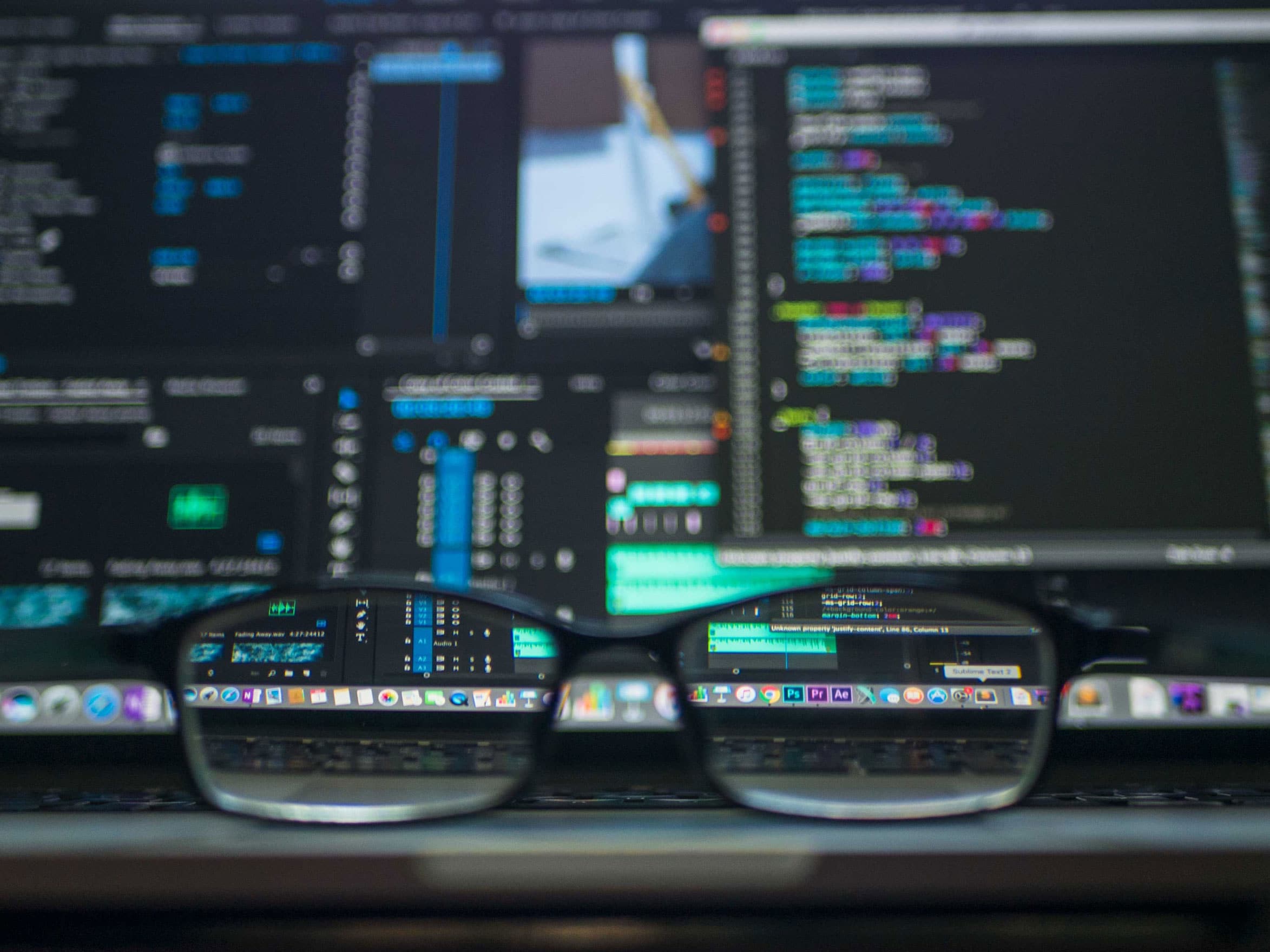 Picture of computer monitors with code on them and glasses in front