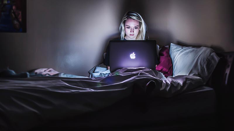 A woman working on a laptop in bed at night to symbolize the importance of knowing how to build a web design side hustle without working to death