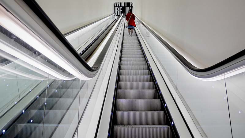 Escalators taking a woman up to symbolize how to grow your side hustle to a million dollar agency