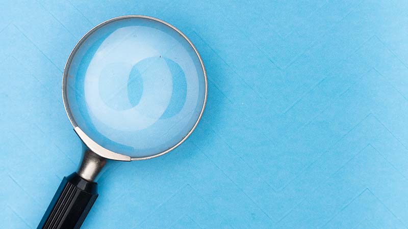 A magnifying glass on a blue background to symbolize how to get freelance clients
