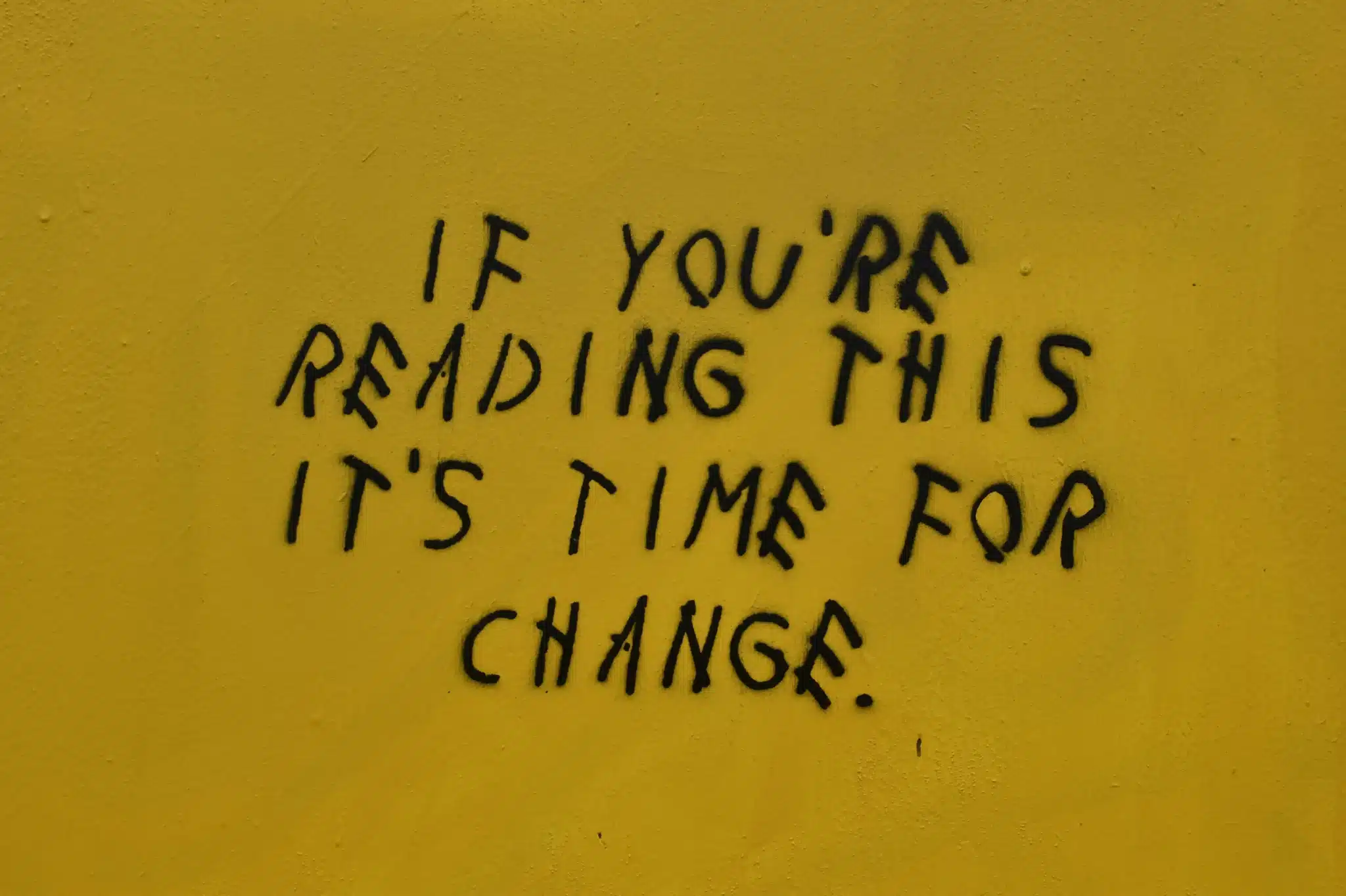 A motivational quote painted in black graffiti-style text on a yellow wall, reading ‘If you’re reading this, it’s time for change.’ A symbolic reminder for those considering how to make a career change in your 30s and take the next step toward a new path