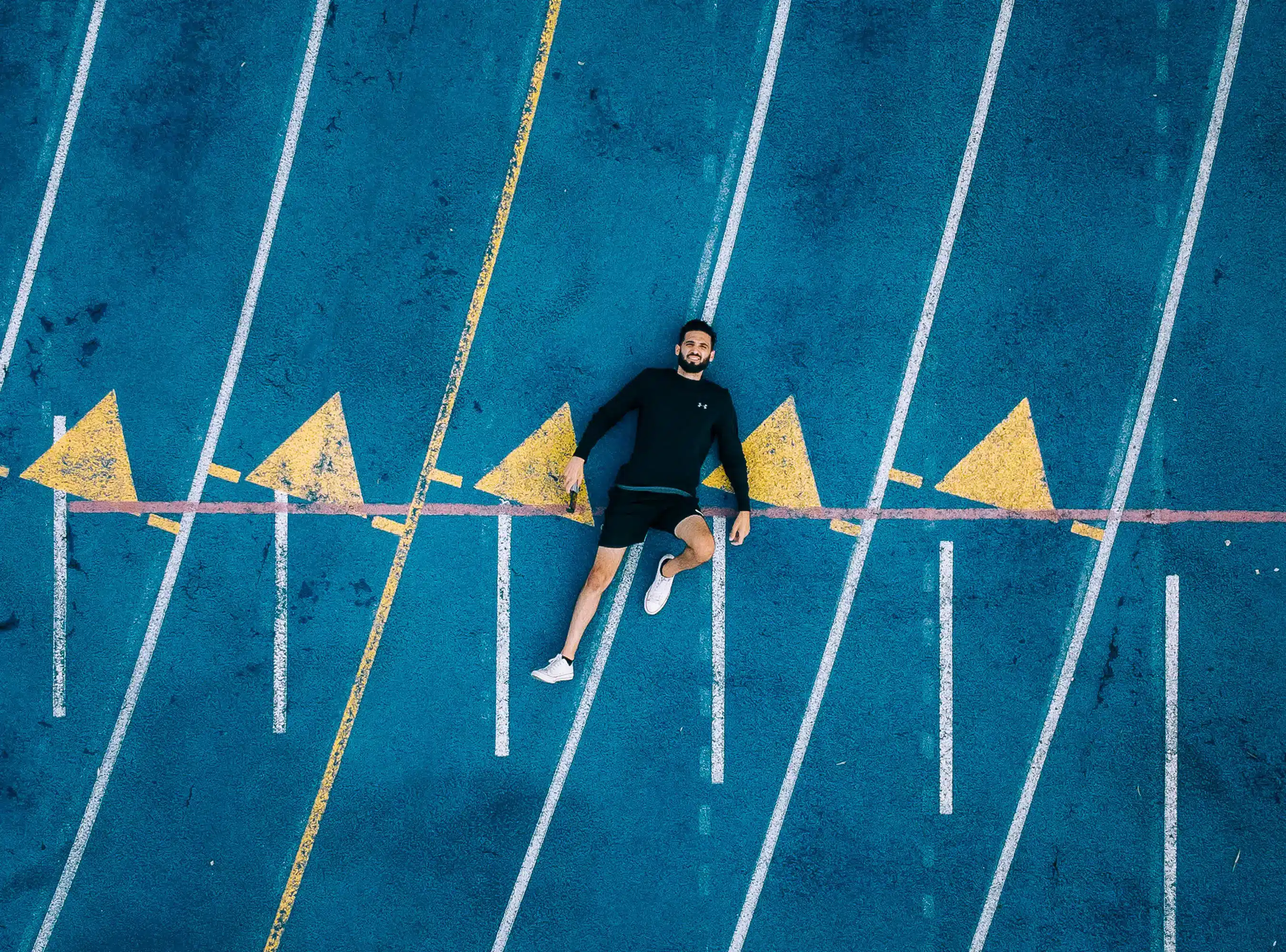 Man lying on a blue track with yellow arrows, representing the journey of starting web design in 2025 with focus and strategy